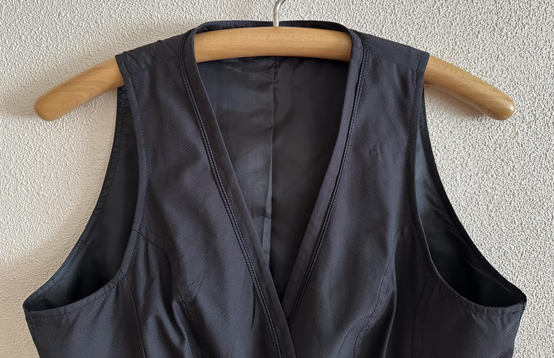 May include: A black sleeveless dress with a V-neckline and a fitted bodice. The dress is made of a smooth, lightweight fabric.