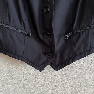 May include: A black sleeveless vest with two zippered pockets on each side and three buttons down the front.