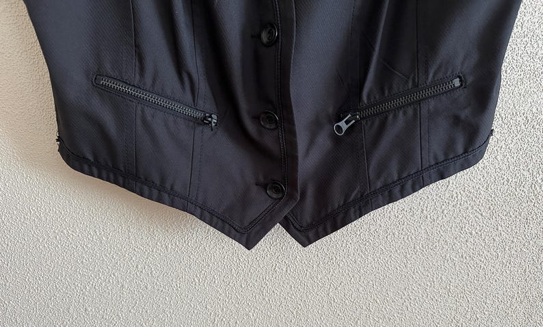 May include: A black sleeveless vest with two zippered pockets on each side and three buttons down the front.