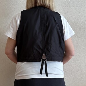 May include: A black sleeveless vest with a tie closure in the back. The vest is made of a smooth, lightweight fabric.