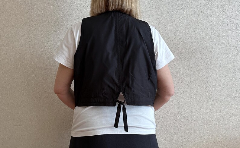 May include: A black sleeveless vest with a tie closure in the back. The vest is made of a smooth, lightweight fabric.