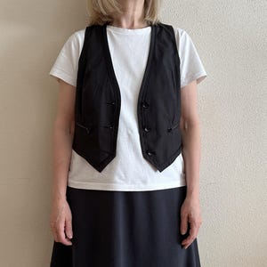 May include: A black sleeveless vest with a white button-up shirt and a black skirt.