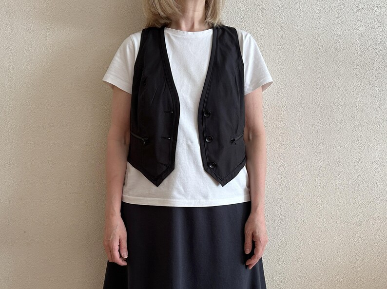 May include: A black sleeveless vest with a white button-up shirt and a black skirt.