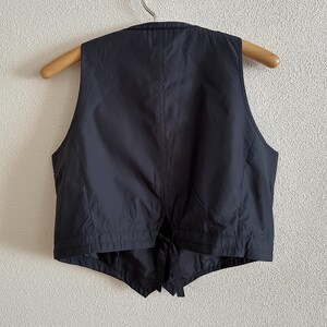 May include: A black sleeveless vest with a tie closure. The vest has a simple design and is made of a smooth fabric.