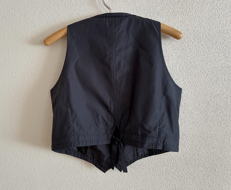 May include: A black sleeveless vest with a tie closure. The vest has a simple design and is made of a smooth fabric.
