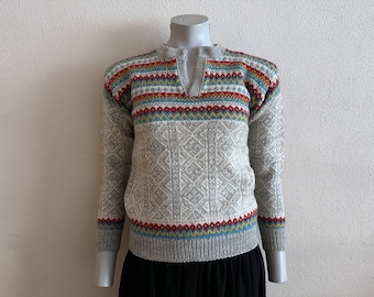 May include: A gray knitted sweater with a colorful geometric pattern around the neck and cuffs. The sweater has a V-neck and long sleeves.