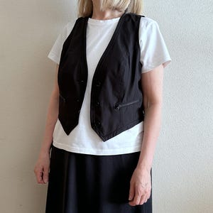 May include: A black sleeveless vest with a white button-up shirt and a black skirt.