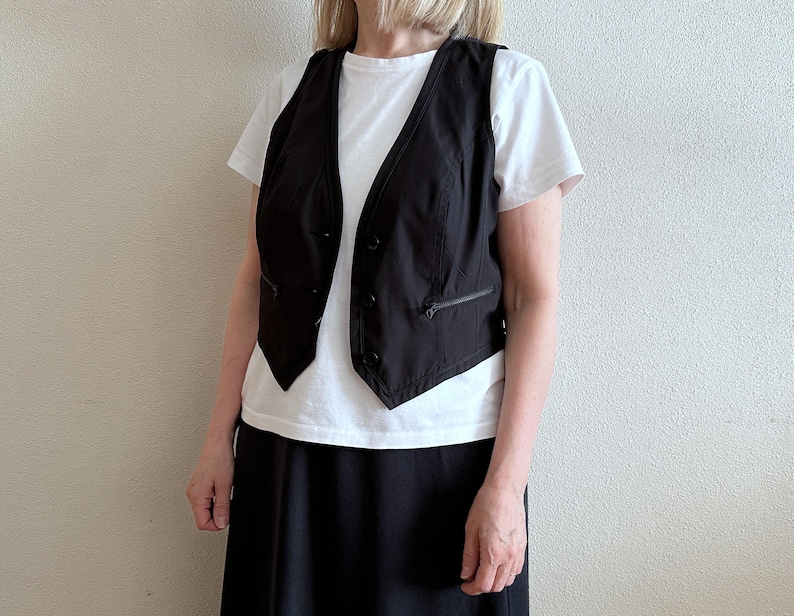May include: A black sleeveless vest with a white button-up shirt and a black skirt.