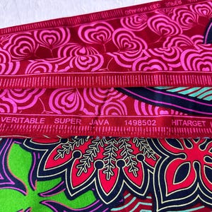以下が含まれることがあります： 赤とピンクの生地に花柄がプリントされています。生地には「VERITABLE SUPER JAVA 1498502 HITarget」という文字が印刷されています。