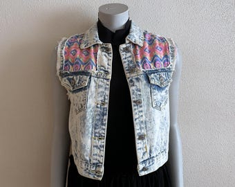 May include: A light blue denim vest with a colorful patterned fabric on the shoulders. The vest has a distressed look and is unbuttoned.