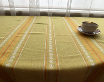May include: A green tablecloth with orange and white stripes. The tablecloth has a pattern of small white circles along the stripes. A white coffee cup with a gold rim sits on a white saucer on the tablecloth.
