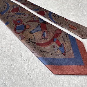 May include: A patterned necktie with a brown base color and abstract shapes in red, blue, and black. The tie has a blue and rust-colored border. The design is artistic and eye-catching.
