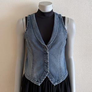 以下が含まれることがあります： 尖った襟とボタン留めが特徴の青いデニムベスト。ベストはクラシックなデザインで、袖なしです。