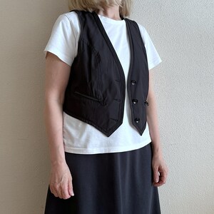 May include: A black vest with a white shirt and a black skirt. The vest has a button closure and a pocket on the left side.