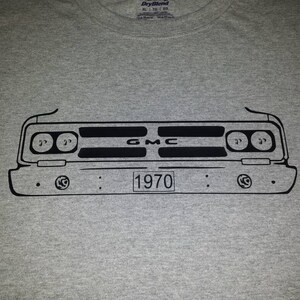 Puede incluir: Una camiseta gris con un contorno negro de una parrilla delantera de un cami&oacute;n GMC 1970. La parrilla tiene el texto "GMC" y "1970" impreso en ella.