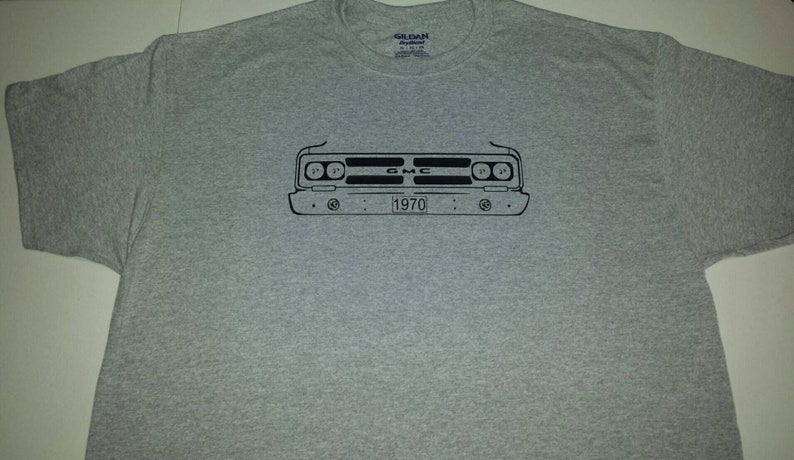 Puede incluir: Una camiseta gris con un contorno negro de la parte delantera de un cami&oacute;n GMC de 1970. El cami&oacute;n tiene una parrilla negra con el texto "GMC" y una placa de matr&iacute;cula que dice "1970".