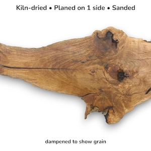 Puede incluir: Una pieza de madera secada al horno, cepillada y lijada, que muestra la veta. La madera es de color marrón cálido con nudos naturales y una forma única. El texto de la imagen dice: "Kiln-dried • Planed on 1 side • Sanded" y "dampened to show grain."