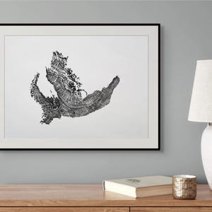 Könnte beinhalten: Ein gerahmter Kunstdruck mit einem schwarz-weißen Tintenabdruck eines Baumquerschnitts. Der Druck zeigt die komplexen, organischen Jahresringe und die texturierte Maserung des Holzes, zentriert in einem schlichten schwarzen Rahmen an einer Wand.