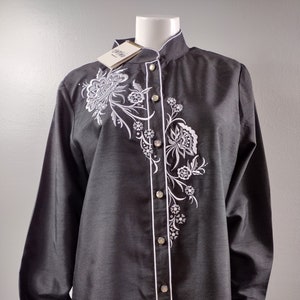 May include: A black long-sleeve button-up shirt with a white floral embroidery design. The shirt has a mandarin collar and a white trim along the front placket and cuffs.