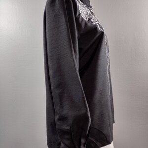 May include: A black long-sleeve shirt with a white embroidered design on the front. The shirt has a mandarin collar and a button-up closure.