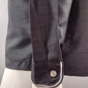 May include: A black long-sleeved shirt with a white trim around the cuffs. The shirt has a button on the cuff.