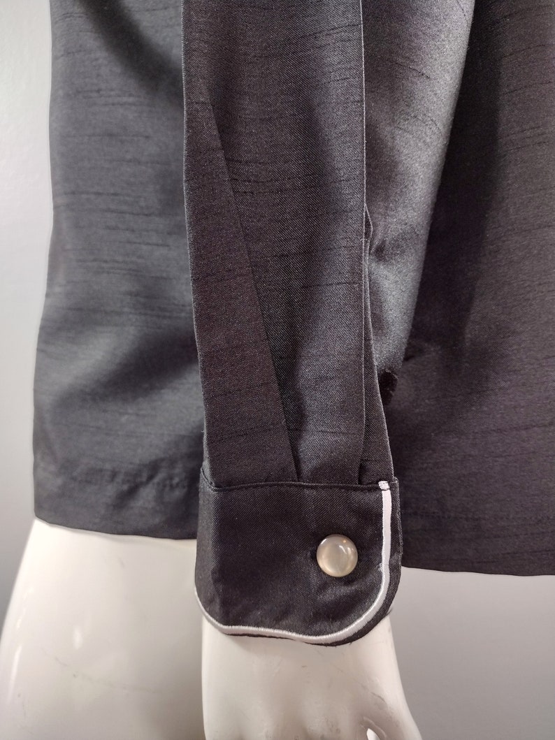 May include: A black long-sleeved shirt with a white trim around the cuffs. The shirt has a button on the cuff.
