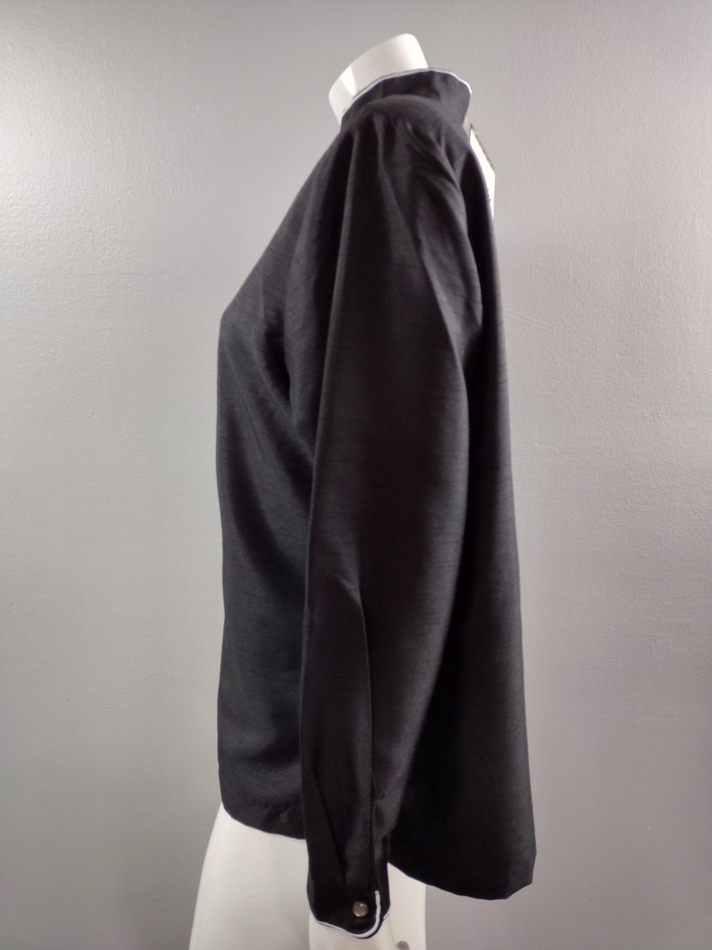 May include: A black long-sleeved shirt with a white collar and cuffs. The shirt has a slightly loose fit and is made of a smooth, silky fabric.