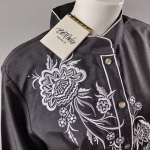 May include: A black long-sleeved shirt with a white embroidered floral design. The shirt has a mandarin collar and a single button closure. The tag on the shirt reads "Bob Mackie Wearable Art."