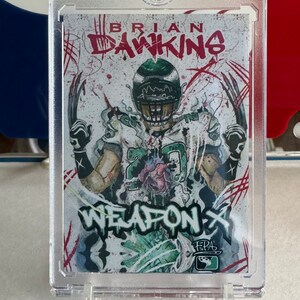 May include: A green and white football card with a drawing of a football player wearing a helmet and jersey. The card has the words "BRIAN DAWKINS" and "WEAPON X" on it. The card is in a plastic case.