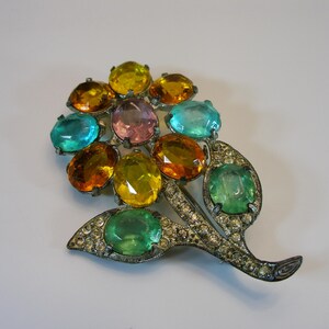 Può includere: Spilla vintage a forma di fiore, con un gruppo di pietre preziose ovali colorate nelle tonalità del giallo, arancione, verde acqua e rosa. La spilla ha uno stelo e foglie in metallo argentato, impreziositi da piccoli strass trasparenti.