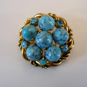 Puede incluir: Broche vintage con piedras turquesas veteadas engastadas en un marco de metal dorado. El broche tiene un diseño circular con un borde retorcido en forma de cuerda, y las piedras están dispuestas en un patrón floral.