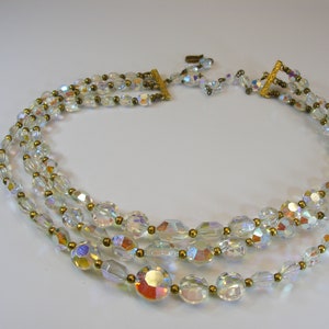 May include: A three-strand iridescent crystal necklace with gold-toned beads and a clasp.
