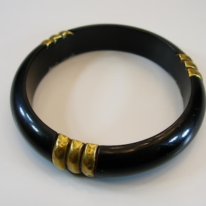 May include: A black bangle bracelet with gold accents. The bracelet is made of a smooth, shiny material and has a simple, elegant design.