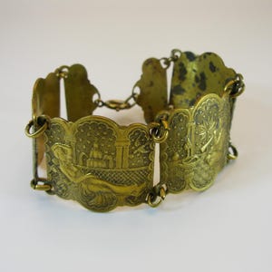 May include: A vintage gold-coloured bracelet with detailed, ornate designs. The bracelet comprises several rectangular panels linked by small chains. Each panel displays a different embossed scene, including figures and architectural elements.