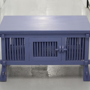 May include: A blue wooden coffee table with a slatted door and a solid top. The table has a simple design with a rectangular shape and four legs.