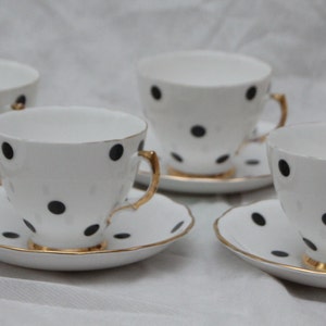 Puede incluir: Juego de seis tazas de té y platillos blancos con lunares negros y ribete dorado.