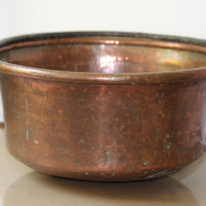 May include: A large copper pot with two iron handles. The pot has a worn, aged patina and is likely antique.