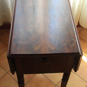 Puede incluir: Una mesa de madera de color marr&oacute;n oscuro con una solapa abatible y patas torneadas. La mesa est&aacute; sobre un suelo de baldosas.