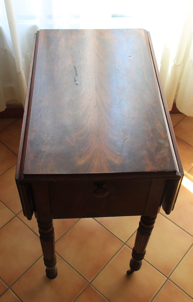 Puede incluir: Una mesa de madera de color marr&oacute;n oscuro con una solapa abatible y patas torneadas. La mesa est&aacute; sobre un suelo de baldosas.