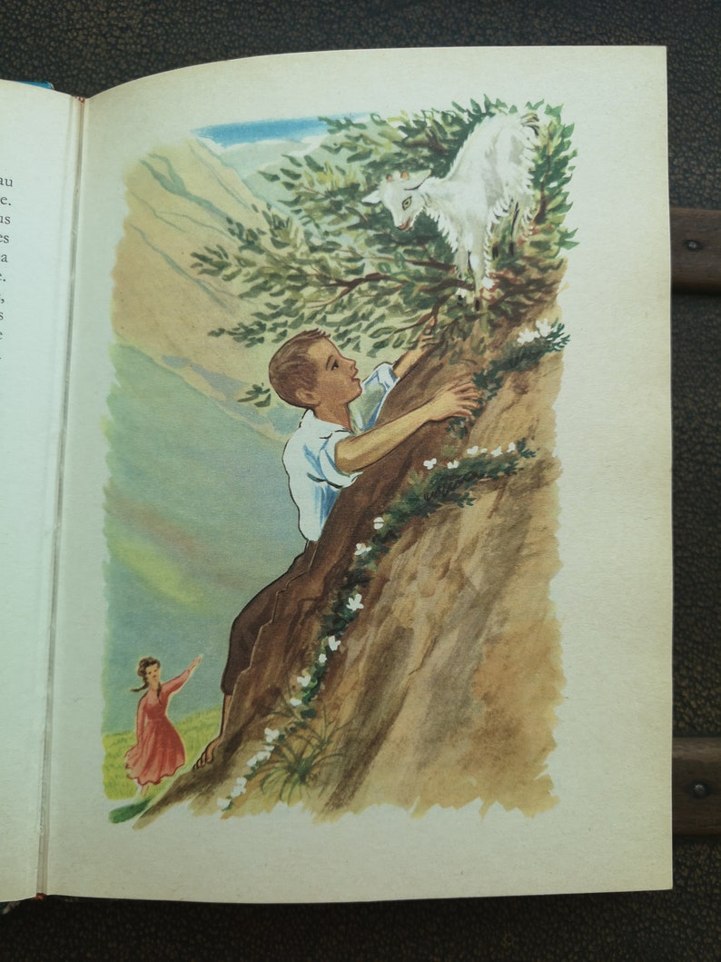 May include: A boy climbs a rocky cliff while reaching for a white goat perched on a branch. A girl in a red dress stands on the ground below.