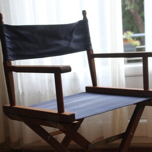May include: A wooden director's chair with a dark blue canvas seat and back. The chair is folded and has a white background.