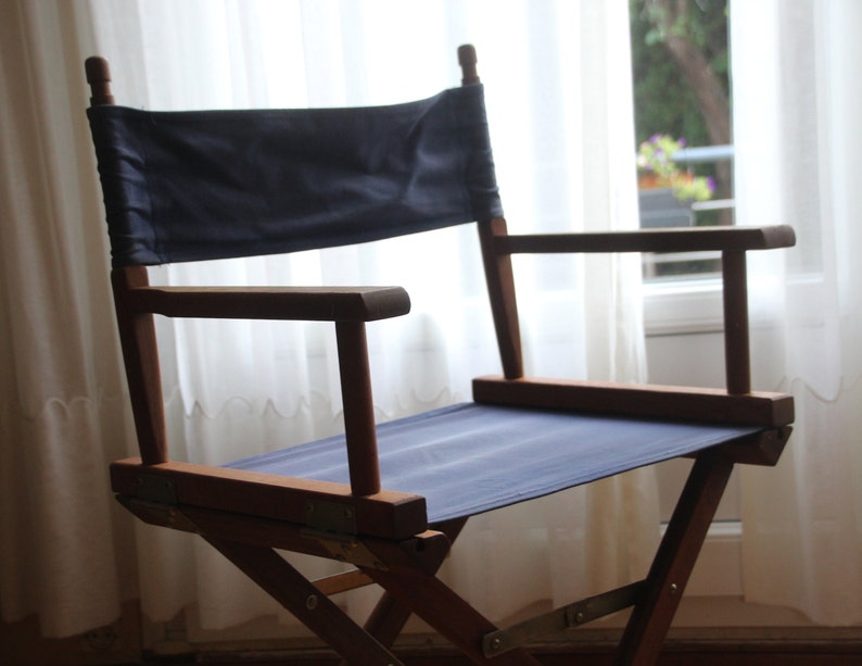 May include: A wooden director's chair with a dark blue canvas seat and back. The chair is folded and has a white background.