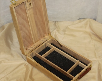 May include: An open wooden box with a black foam interior. The box has a hinged lid and a brass handle. The box is divided into compartments for storing small items.