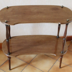 Op de afbeelding: Een houten bijzettafel met twee niveaus met een gebogen bovenblad en een onderblad. De tafel heeft een donkerbruine afwerking en messing accenten op de poten en hoeken.