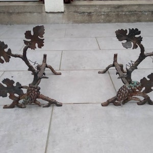 Puede incluir: Un par de soportes para chimenea decorativos de hierro fundido con forma de vides con hojas y uvas. Los soportes son de color marrón oscuro y tienen un acabado rústico.