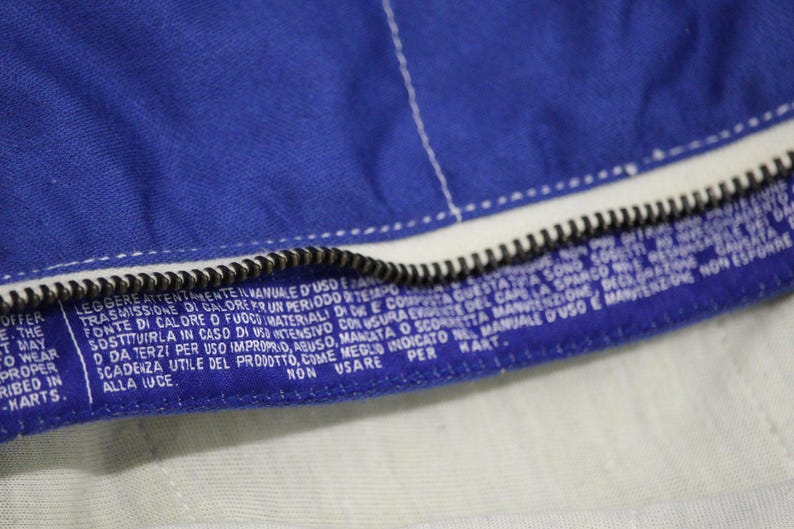 May include: Close-up of a blue fabric with a white zipper and white stitching. The fabric has a label with white text. The text includes the words "offer", "wear", and "kart".
