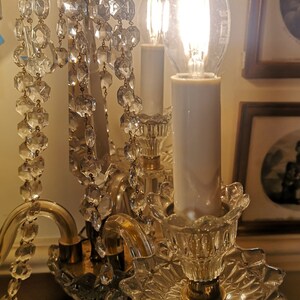 May include: A vintage crystal chandelier with multiple candle-shaped light bulbs. The chandelier features hanging crystal accents and ornate glass detailing. The light bulbs are lit, casting a warm glow. The fixture is likely made of glass and metal.