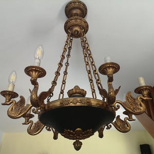 Könnte beinhalten: Verzierter goldener Kronleuchter mit schwanförmigen Armen und einem dunkelgrünen schalenförmigen Zentrum. Der Kronleuchter hat sechs Leuchten und wird mit Ketten von der Decke abgehängt. Ein elegantes Einrichtungsstück.