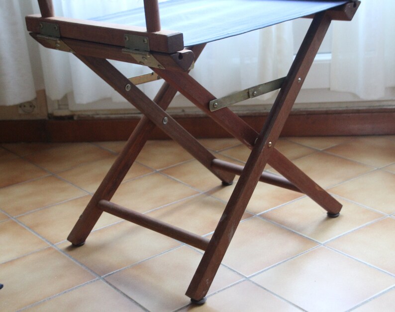 May include: A wooden folding chair with a dark blue canvas seat. The chair is made of dark brown wood and has a simple, classic design.