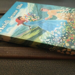 May include: A vintage book titled "Heidi jeune fille" by Flammarion, featuring a colorful illustration of a girl in a blue dress walking through a field of flowers.